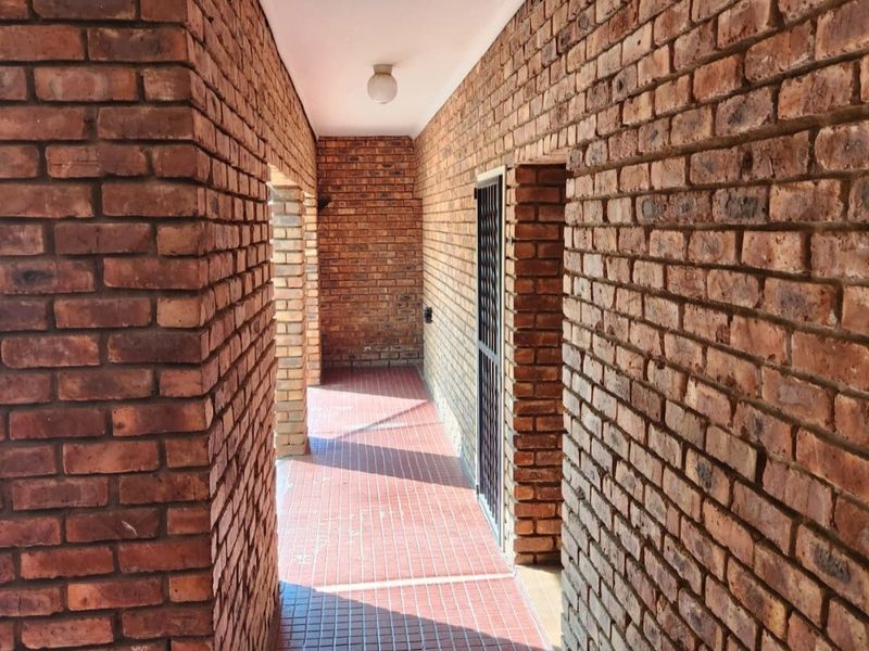 A covered outdoor walkway featuring rustic exposed brick walls and durable tiled flooring, providing a sheltered transition area between building sections.