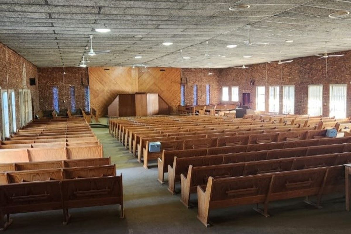 Large hall featuring exposed brick walls, a built-in wooden stage, and acoustic tile ceiling, suitable for community gatherings or events.