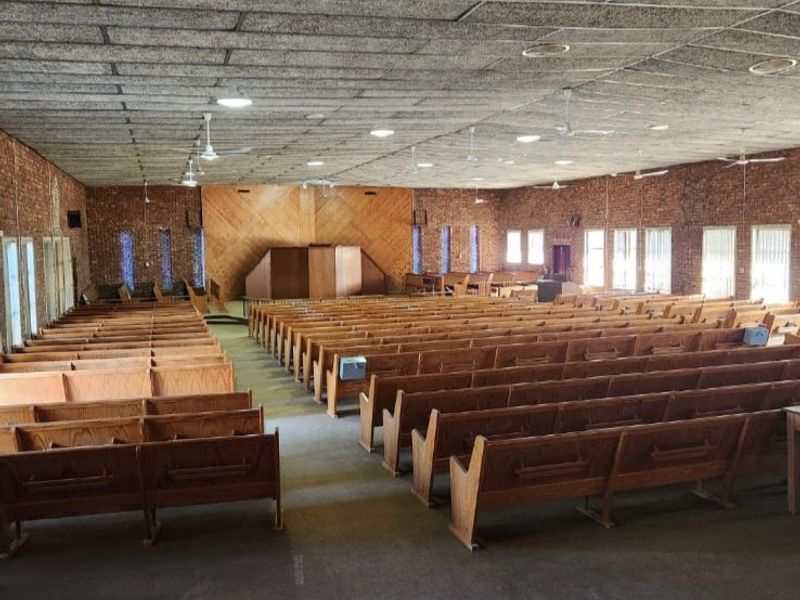 Large hall featuring exposed brick walls, a built-in wooden stage, and acoustic tile ceiling, suitable for community gatherings or events.