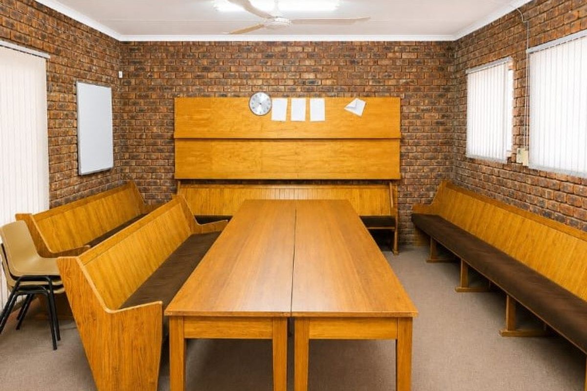 A functional multi-purpose room featuring exposed brick walls, a ceiling fan, and vertical blinds, suitable for a meeting or communal space.