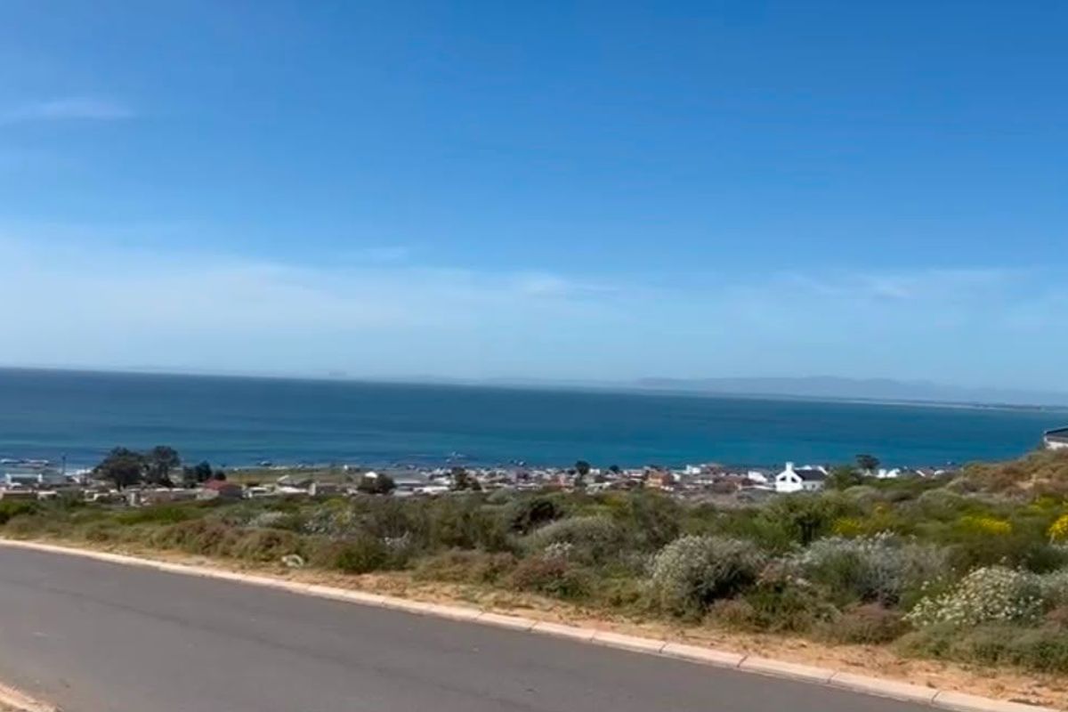 A scenic elevated view overlooking the coastline, ocean, and surrounding residential area from a paved road.