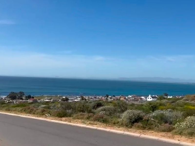 A scenic elevated view overlooking the coastline, ocean, and surrounding residential area from a paved road.