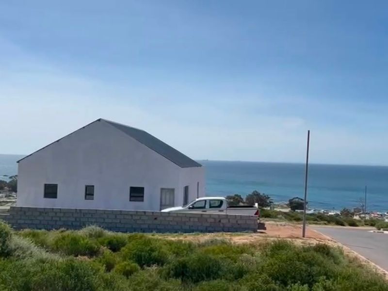 A residential property exterior featuring a simple structure with a pitched roof, enclosed by a concrete block wall, overlooking the ocean.