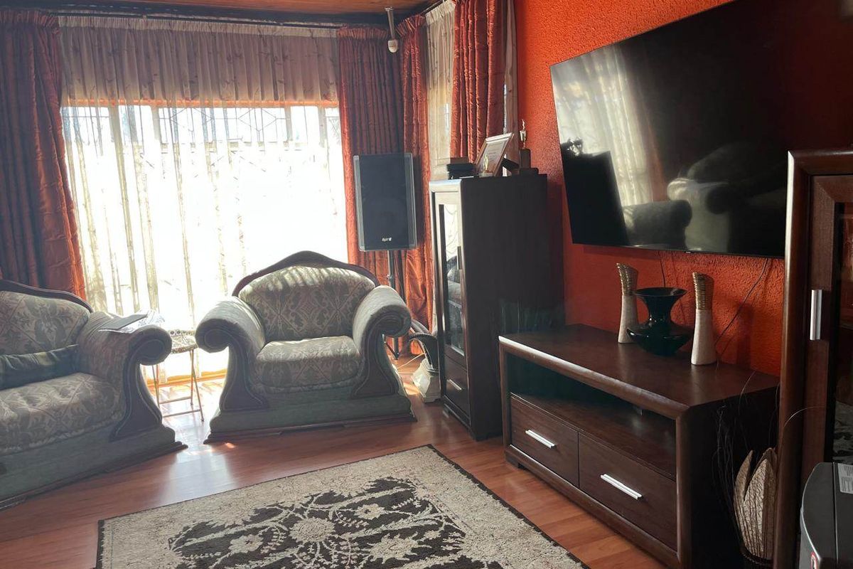 A living room featuring laminate flooring, a timber-paneled ceiling, and textured walls, providing a traditional aesthetic with ample natural light.