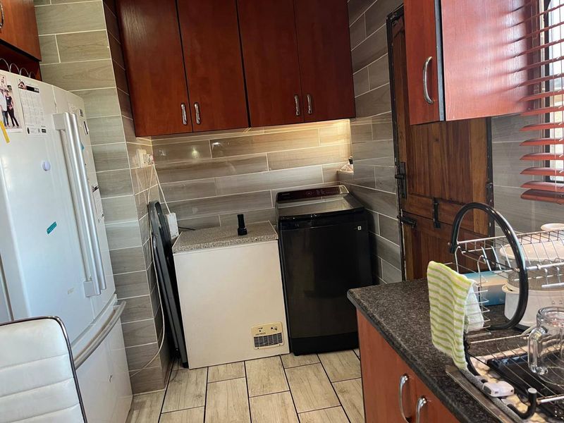 A functional laundry area featuring tiled walls, stone-look countertops, and built-in cabinetry, providing efficient space for laundry appliances and storage.
