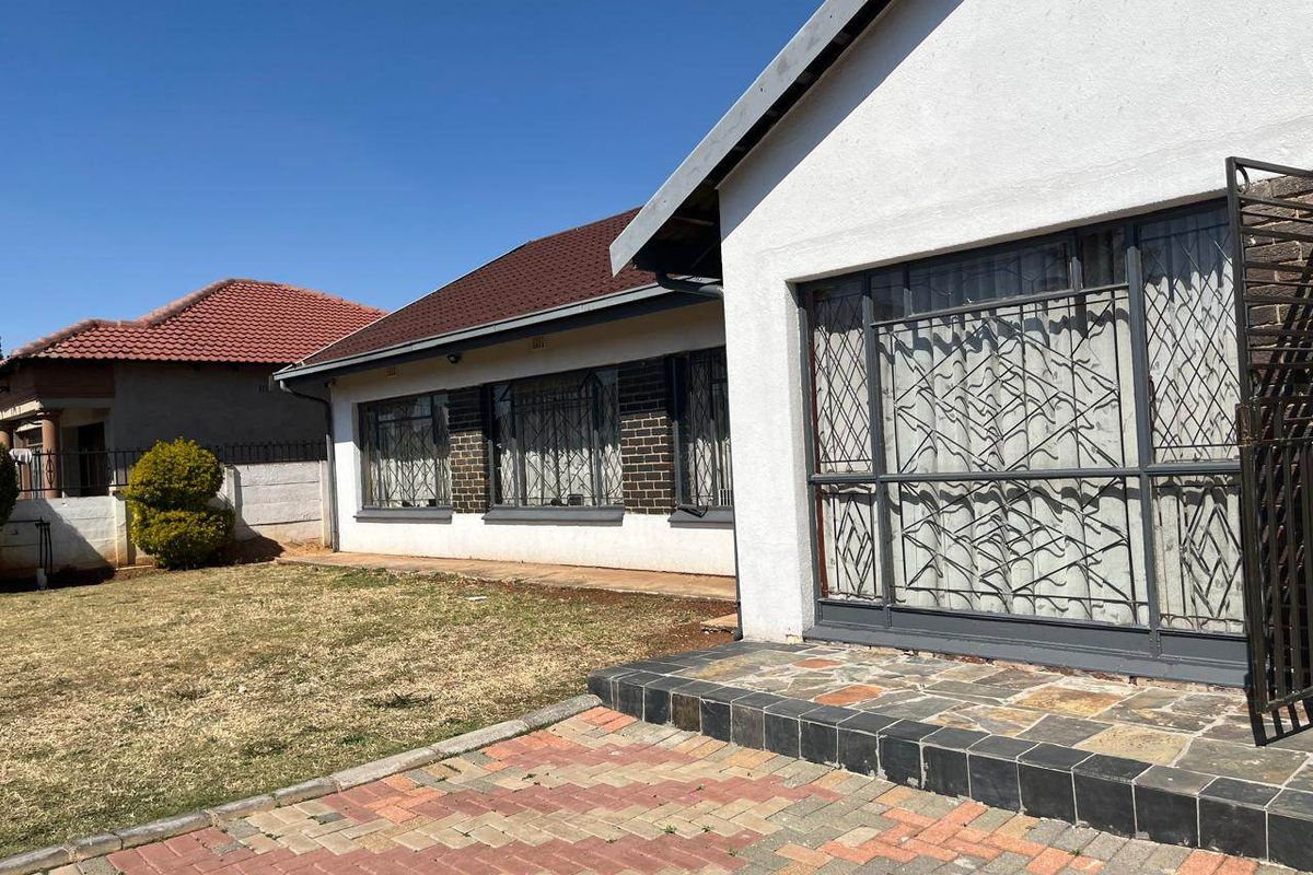 Rear exterior view of the house featuring a paved patio area, lawn, and security-gated windows with a tiled roof.