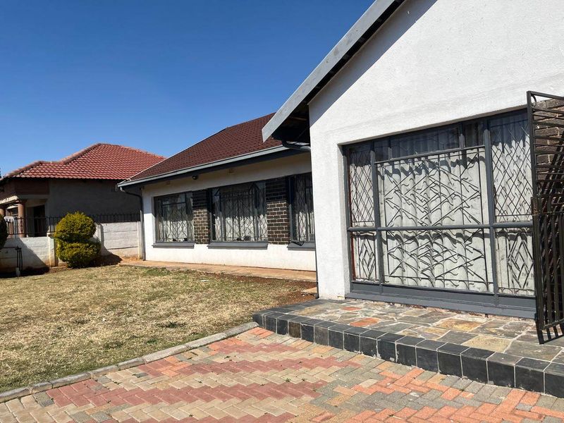 Rear exterior view of the house featuring a paved patio area, lawn, and security-gated windows with a tiled roof.