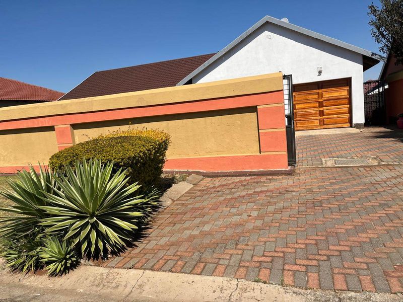 Front view of the property featuring a paved driveway, a secure boundary wall, and a wooden garage door under a tiled roof.