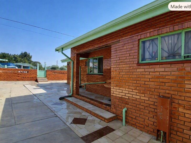 Rear exterior view of a face brick house featuring a paved courtyard, covered patio area, and perimeter walling.