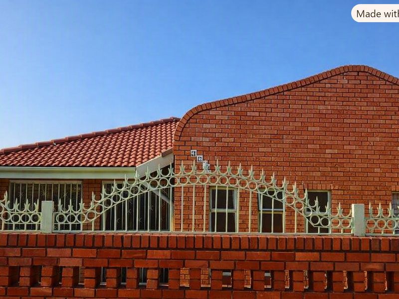 Front elevation of a face brick house featuring a tiled roof and decorative metal perimeter fencing with security bars on the windows.