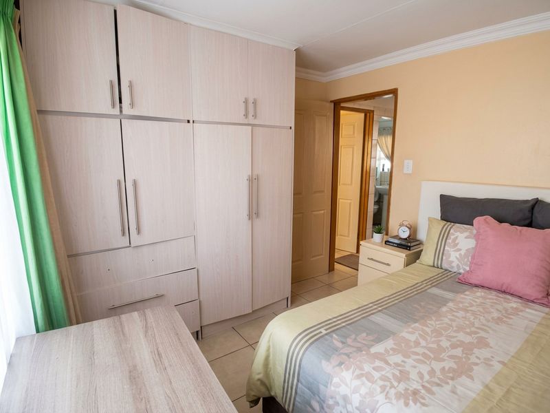 A well-maintained bedroom featuring light wood-finish built-in cupboards, tiled flooring, and coved ceiling details, with direct access to an adjoining room.