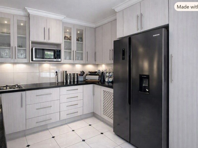 Modern kitchen featuring light wood-grain cabinetry, black granite countertops, built-in microwave, gas hob, and tiled flooring with decorative accents.