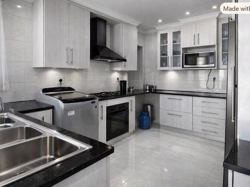 Modern kitchen featuring light wood-grain cabinetry, black granite countertops, integrated appliances, and polished floor tiles with recessed lighting.
