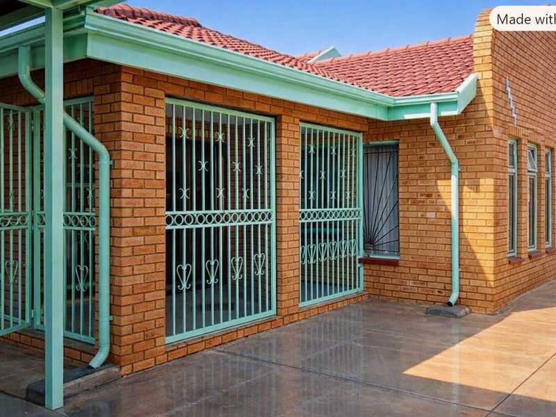 A well-maintained face brick exterior featuring a tiled roof, concrete patio area, and secure metal security gates and window bars.