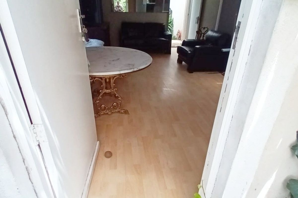 View into a living area featuring laminate flooring and a tiled entrance threshold, showing signs of wear and ceiling damage.