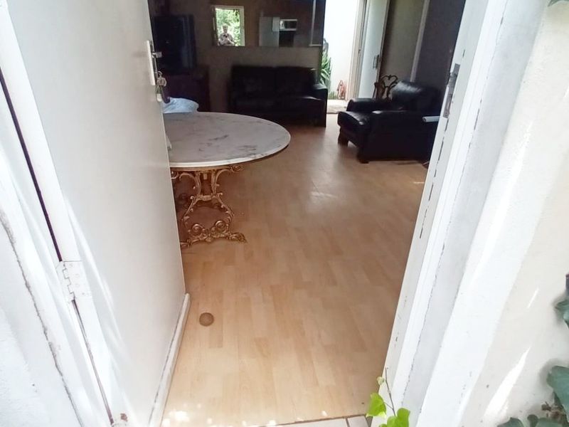 View into a living area featuring laminate flooring and a tiled entrance threshold, showing signs of wear and ceiling damage.