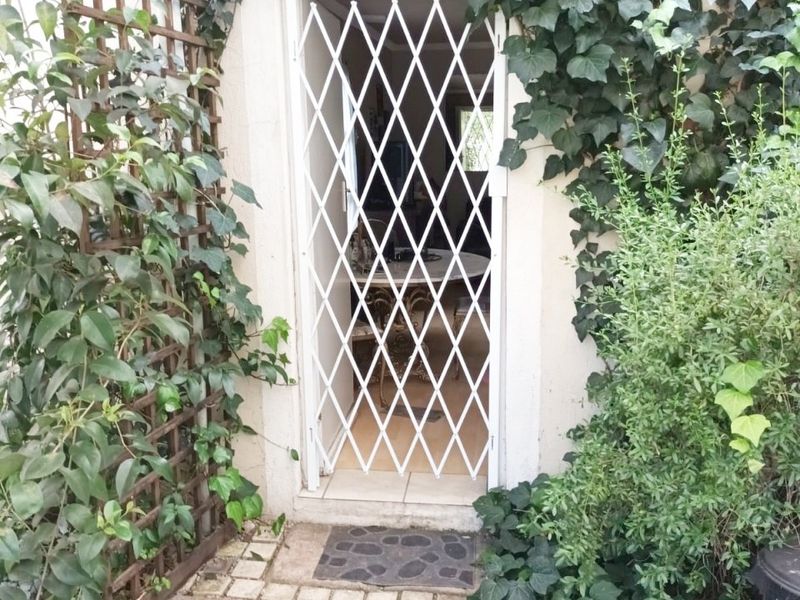A rear entrance featuring a white security gate, surrounded by climbing ivy and established garden greenery with paved access.