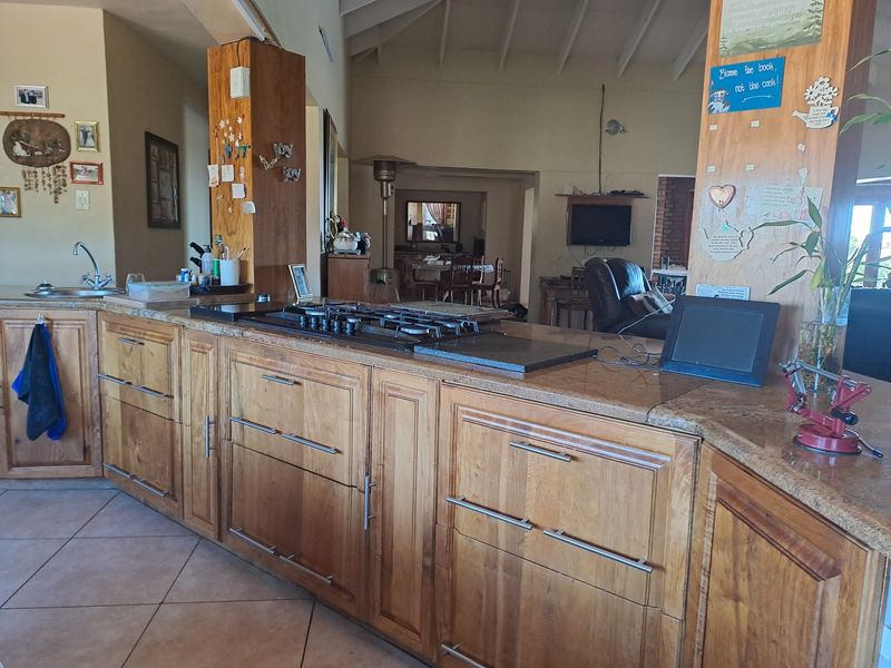 Open-plan kitchen area featuring wooden cabinetry, granite countertops, and a gas hob, flowing into the adjacent living and dining spaces under a vaulted ceiling.