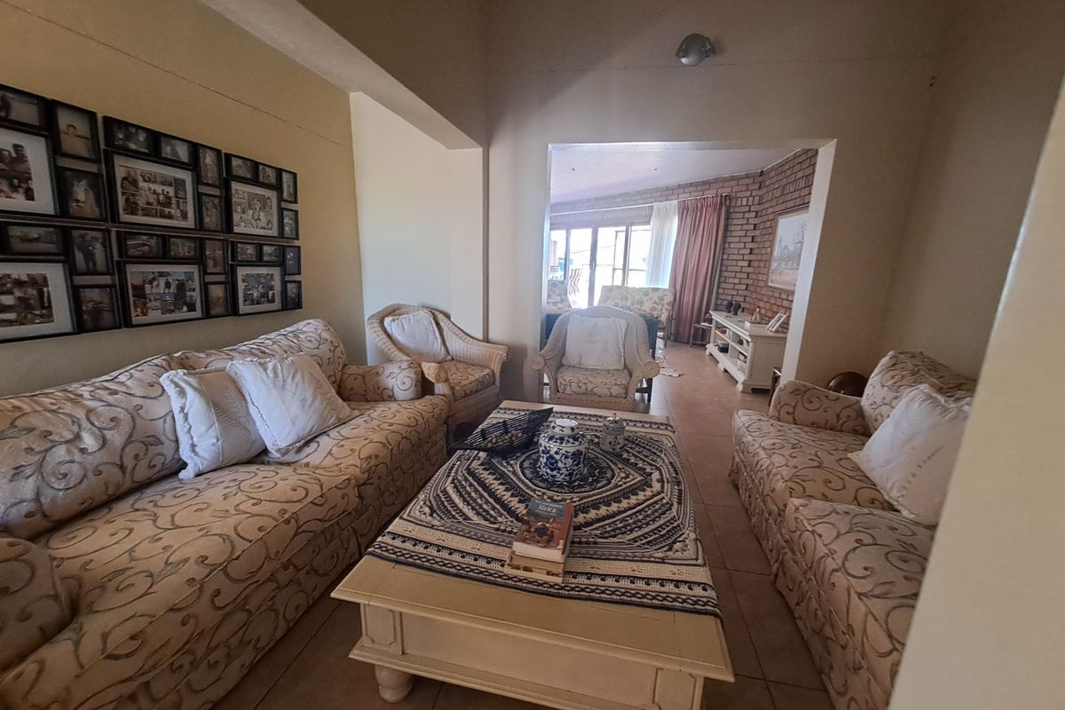 A comfortable living room featuring tiled flooring and an exposed brick accent wall, leading into an adjacent sunroom area.