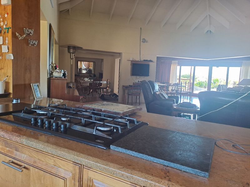 Spacious open-plan living area featuring a vaulted ceiling with exposed rafters, a built-in gas hob on the kitchen island, and large sliding glass doors.