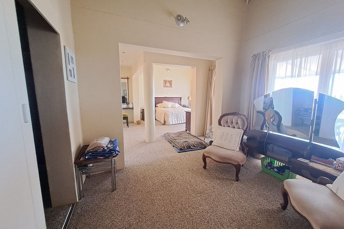 A spacious bedroom featuring a vaulted ceiling, carpeted flooring, and a structural column leading into an adjoining sleeping area.