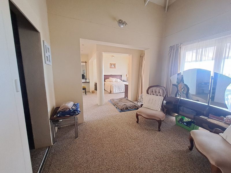 A spacious bedroom featuring a vaulted ceiling, carpeted flooring, and a structural column leading into an adjoining sleeping area.