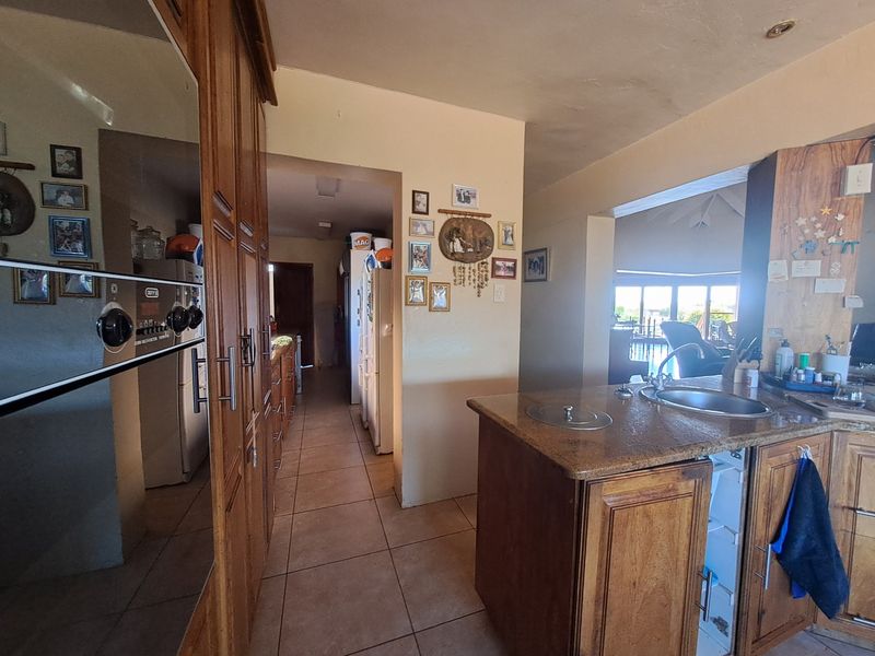 A functional kitchen featuring wooden cabinetry, a central island with a sink, and tiled flooring, with an open-plan layout leading to adjacent living areas.