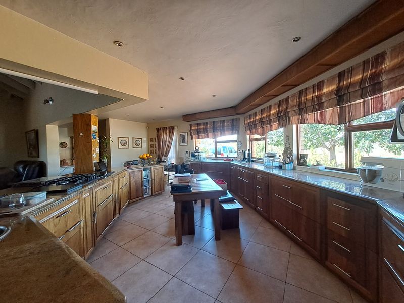 Spacious farmhouse kitchen featuring extensive wooden cabinetry, granite countertops, a built-in gas hob, and large windows overlooking the property grounds.