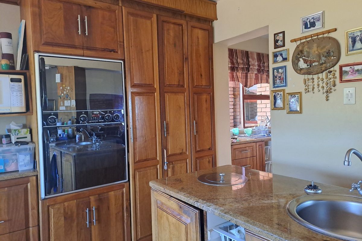 A kitchen featuring warm-toned wooden cabinetry, granite countertops, a built-in oven, and a central island with an integrated sink.