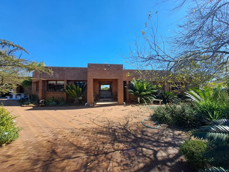 Front elevation of a face brick farm-style residence featuring a paved driveway, established garden landscaping, and a central covered entrance.