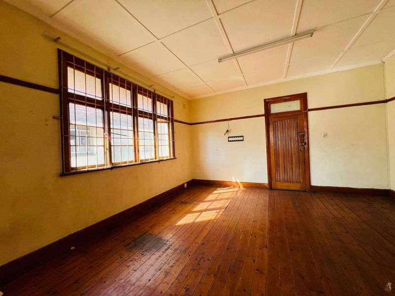 An empty bedroom featuring original timber flooring, timber window frames with security bars, and a classic timber door, ready for renovation.