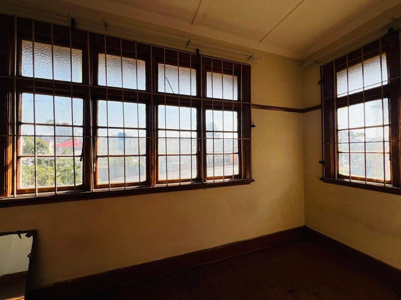 An empty bedroom featuring original timber flooring, classic picture rails, and large timber-framed windows with security bars.