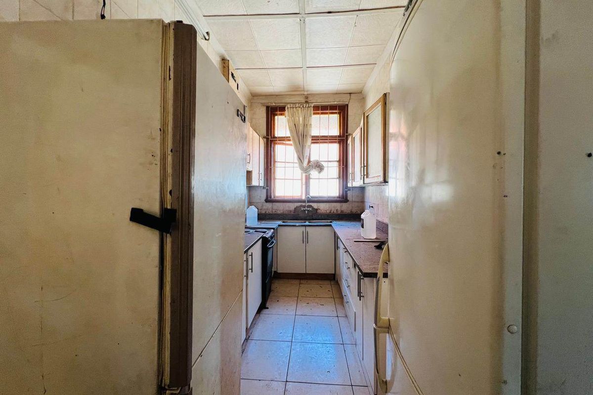 A narrow, dated galley kitchen featuring original cabinetry, tiled flooring, and a drop ceiling, requiring significant modernization and renovation to improve functionality and aesthetic appeal.