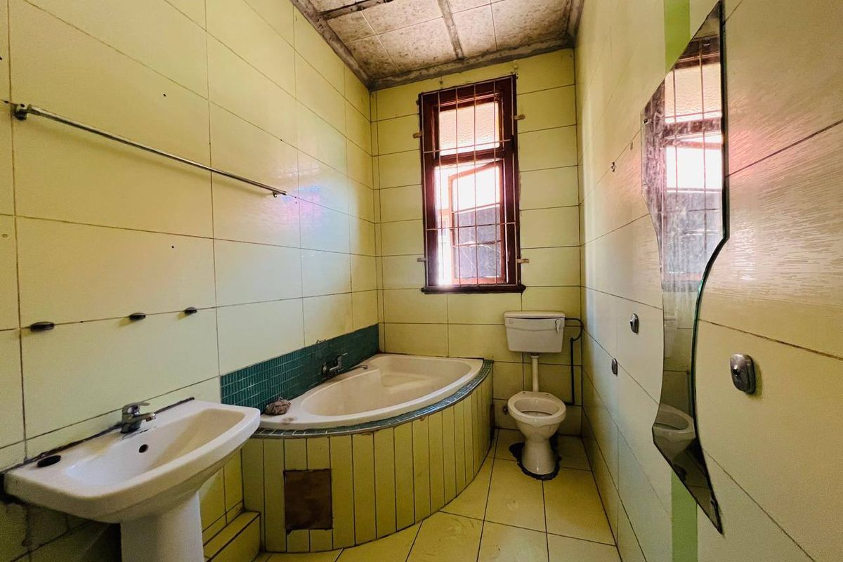 A dated bathroom featuring a pedestal basin, built-in bathtub, and toilet, requiring significant renovation and modernization of finishes.