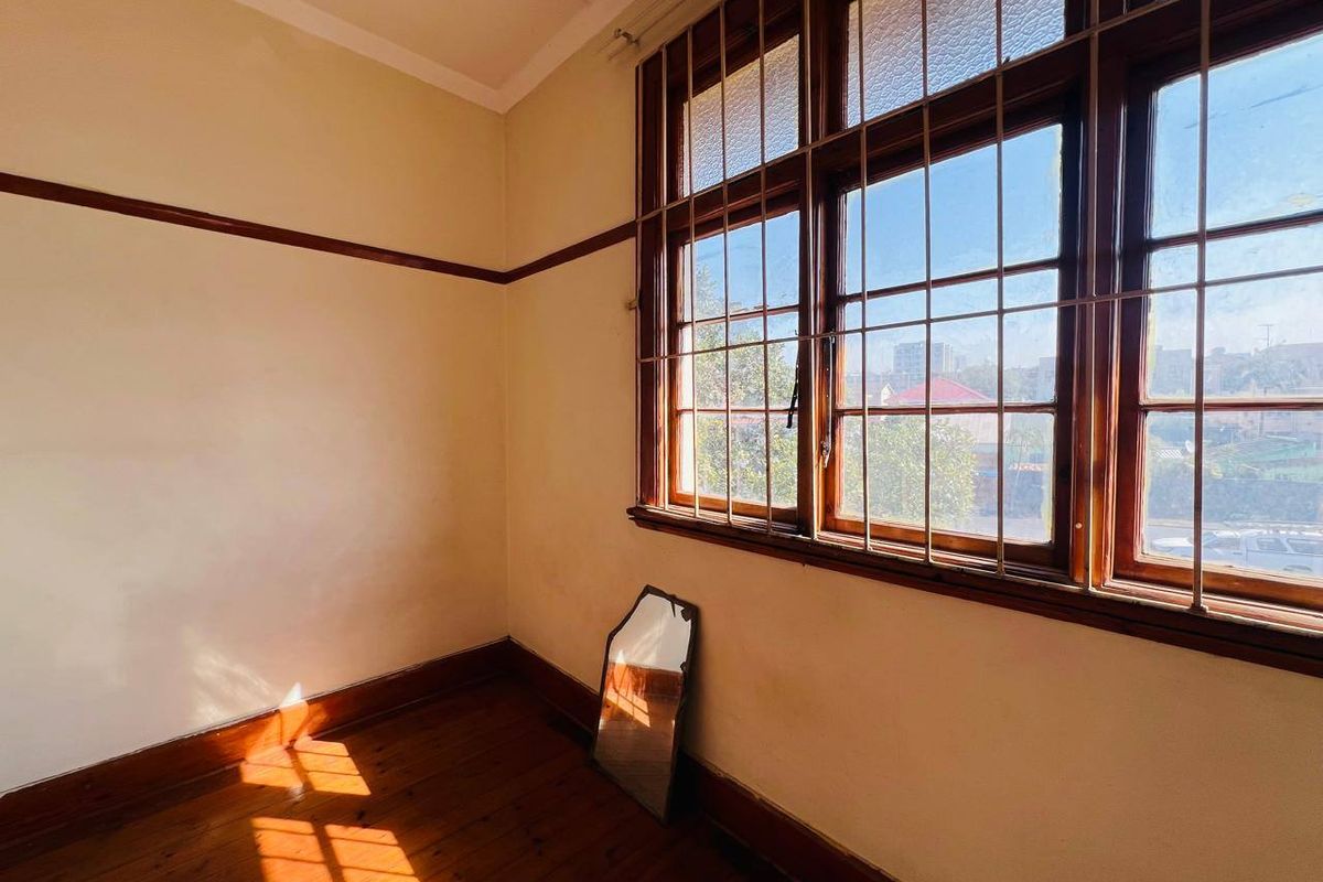 An empty bedroom featuring original timber flooring, picture rails, and large timber-framed windows with security bars, offering a blank canvas for renovation.