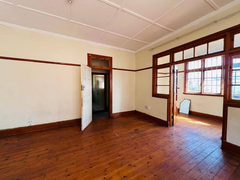 An empty living room featuring original timber flooring, wooden door and window frames, and a classic panelled ceiling, offering a blank canvas for renovation.