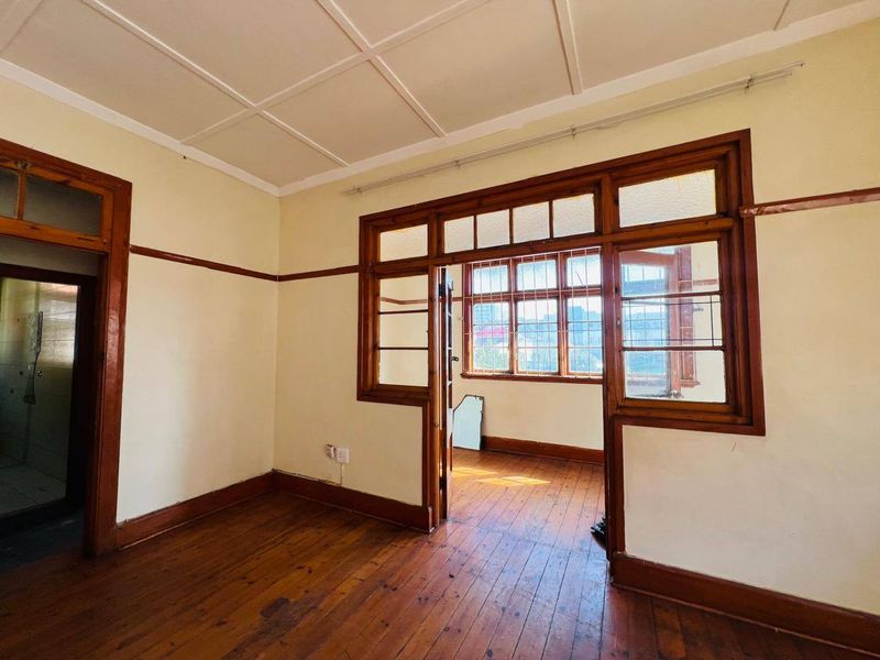 An empty living area featuring original timber flooring, classic wooden door and window frames with leaded glass detailing, and a panelled ceiling.
