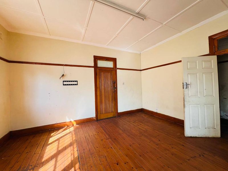 An empty bedroom featuring original timber flooring, a classic timber door with transom, and traditional picture rails, requiring cosmetic updates to restore its charm.