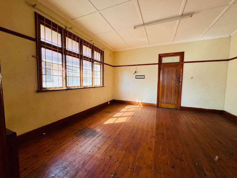 An empty bedroom featuring original timber flooring, timber window frames with security bars, and a classic timber door, requiring cosmetic updates and repairs.