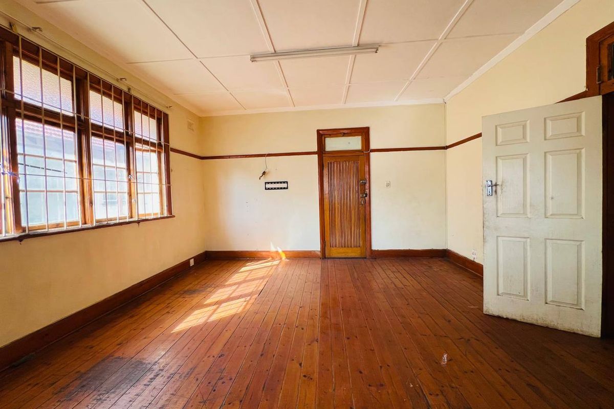 An empty living room featuring original timber flooring, timber window frames with security bars, and a classic timber door.