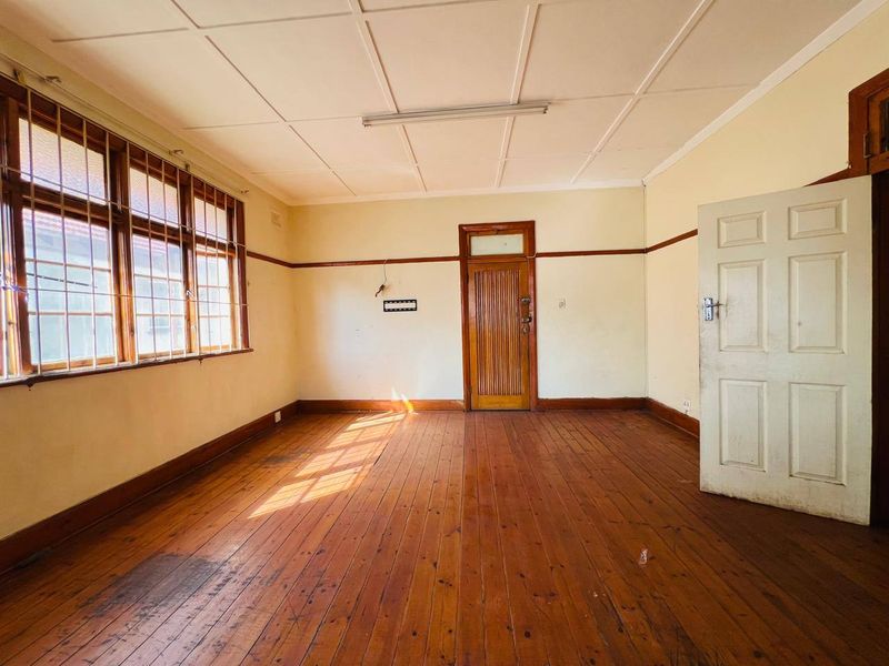 An empty living room featuring original timber flooring, timber window frames with security bars, and a classic timber door.