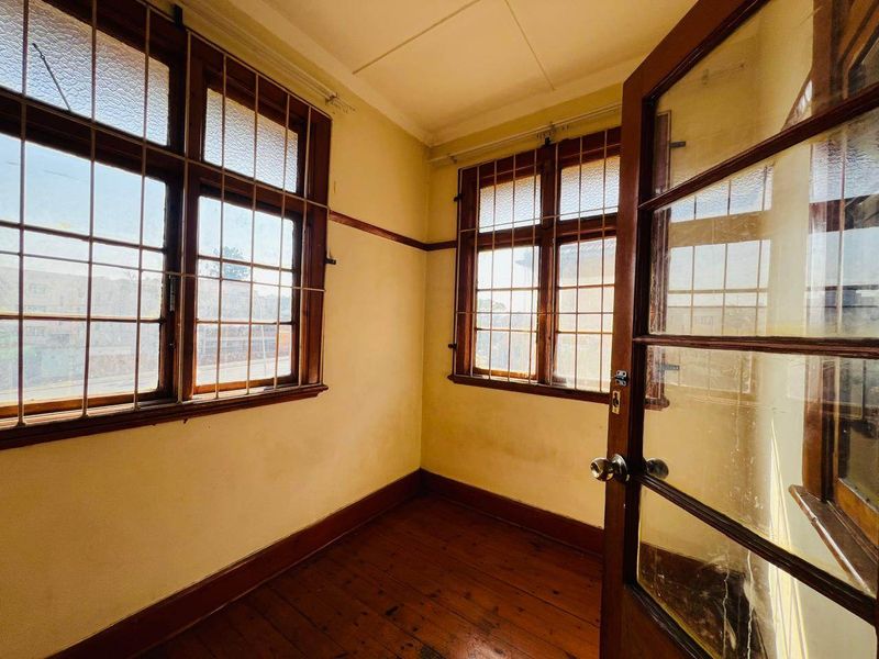 A vacant room featuring original timber flooring, timber-framed windows with security bars, and a classic timber-framed glass door.