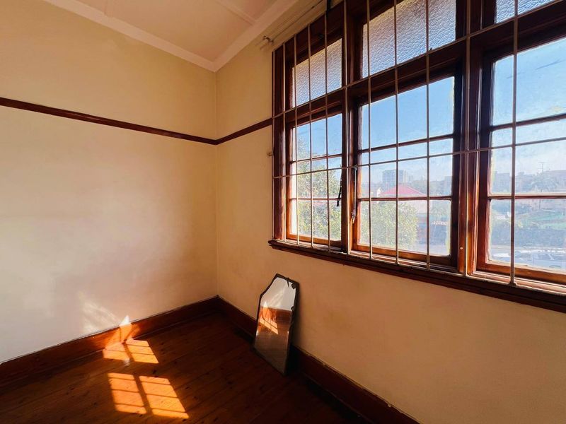 An empty bedroom featuring original timber flooring, picture rails, and large timber-framed windows with security bars, offering a blank canvas for renovation.