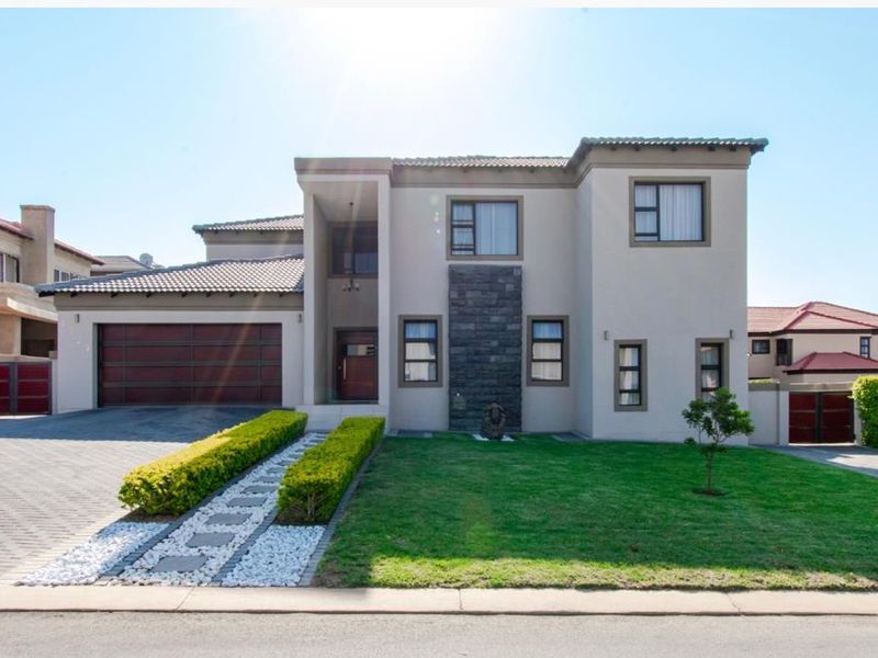 Modern double-story residential property featuring a paved driveway, double garage, and a well-maintained front garden with stone cladding architectural details.