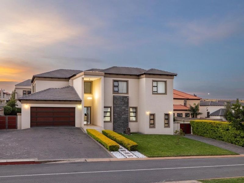 A modern double-story residential property featuring a paved driveway, double garage, stone cladding accents, and a well-maintained front garden.
