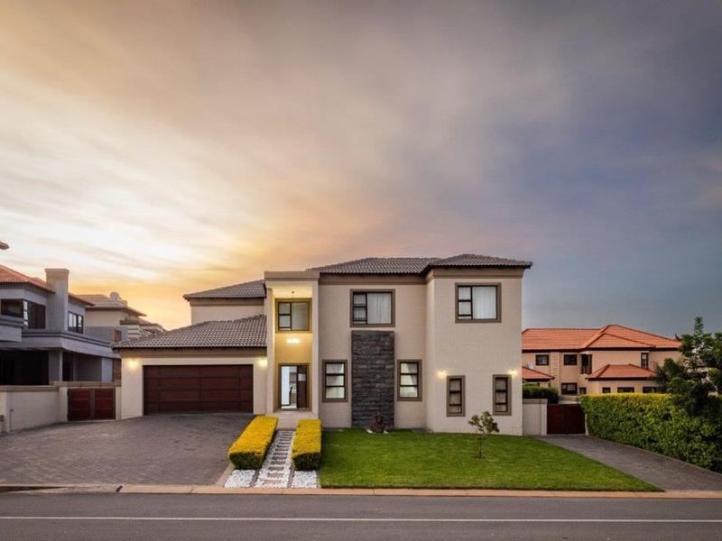 A well-maintained double-story residential property featuring a paved driveway, double garage, stone cladding accents, and a manicured front lawn at sunset.