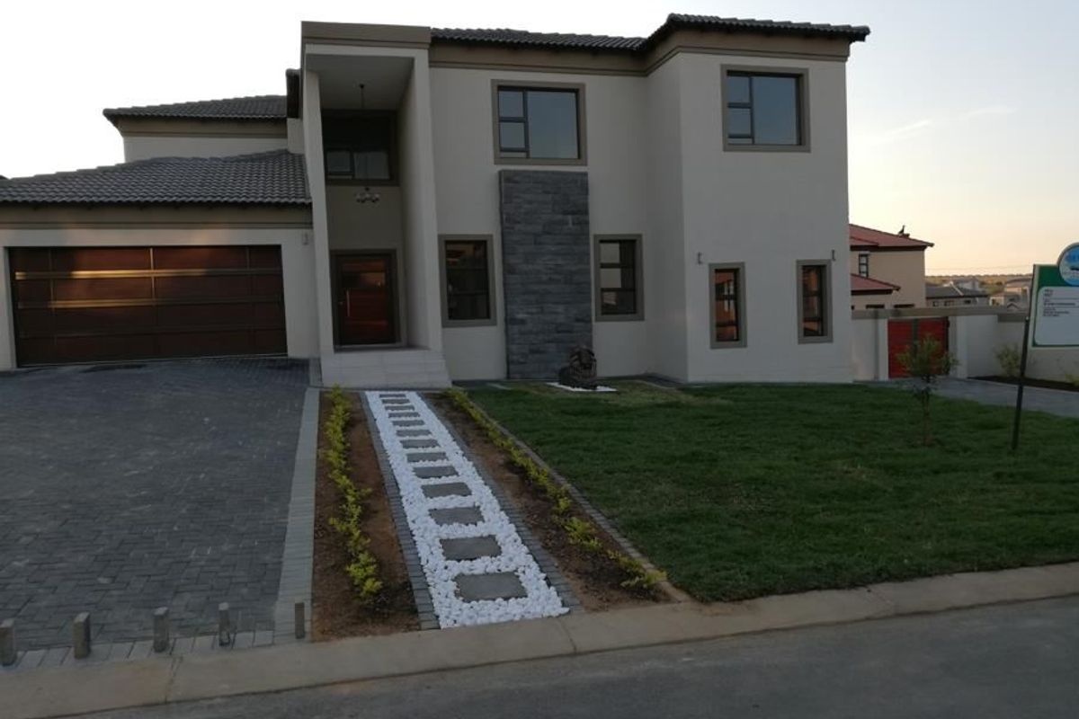 Modern double-story residential property featuring a paved driveway, double garage, stone-clad facade detail, and a well-maintained front garden with a stone pathway.