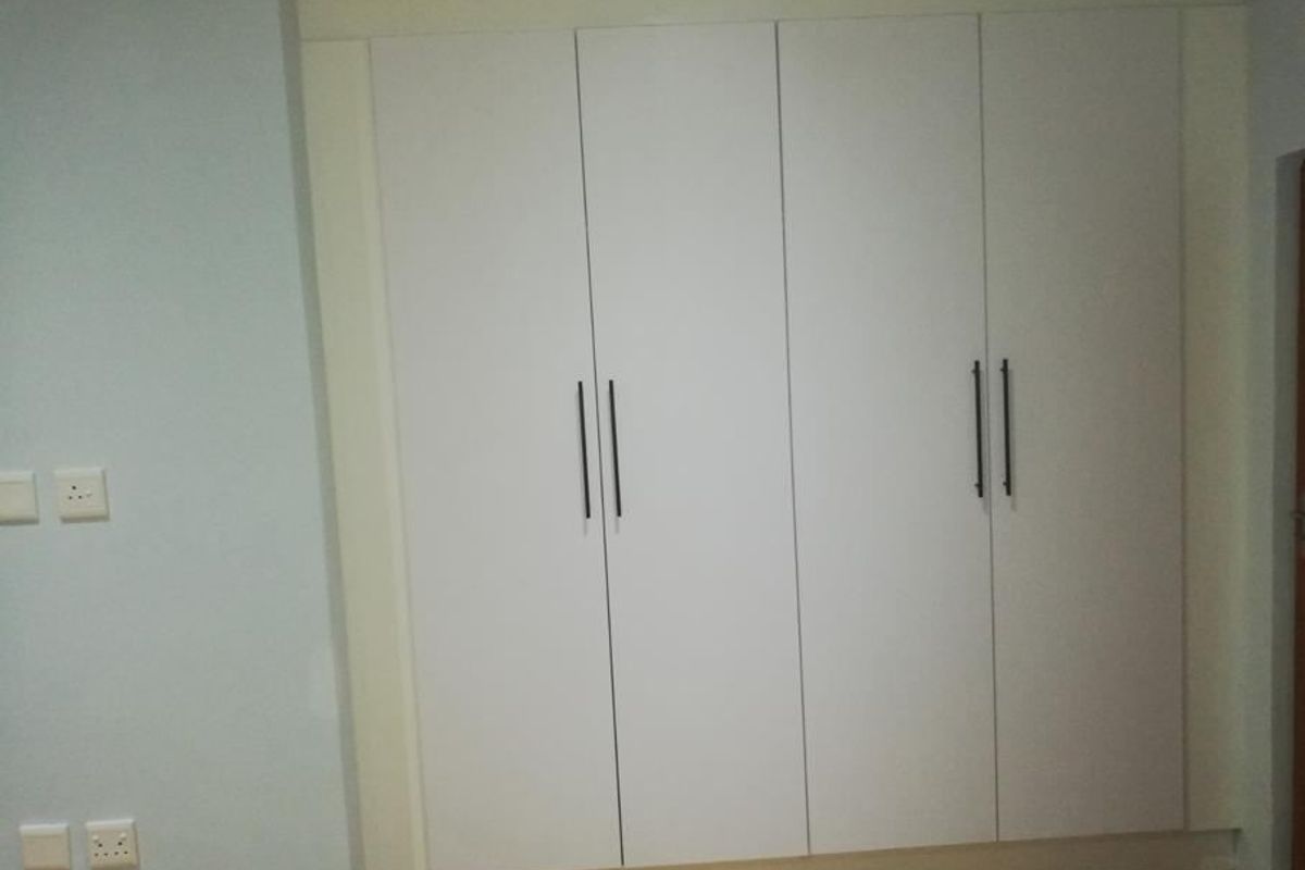 A bedroom featuring modern, white built-in cupboards with sleek black handles, providing ample storage space.