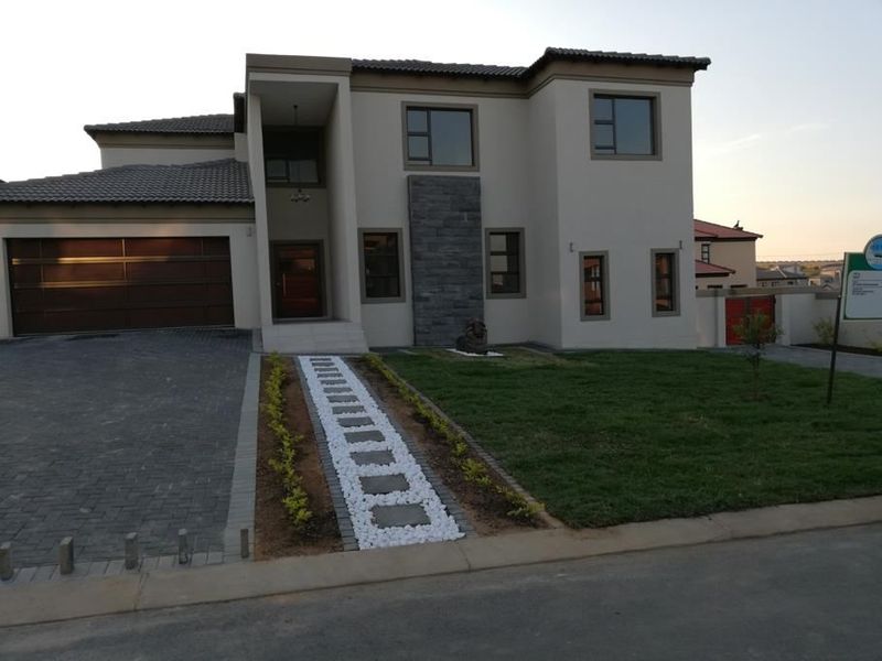 Modern double-story residential property featuring a paved driveway, double garage, stone-clad facade detail, and a well-maintained front garden with a stone pathway.