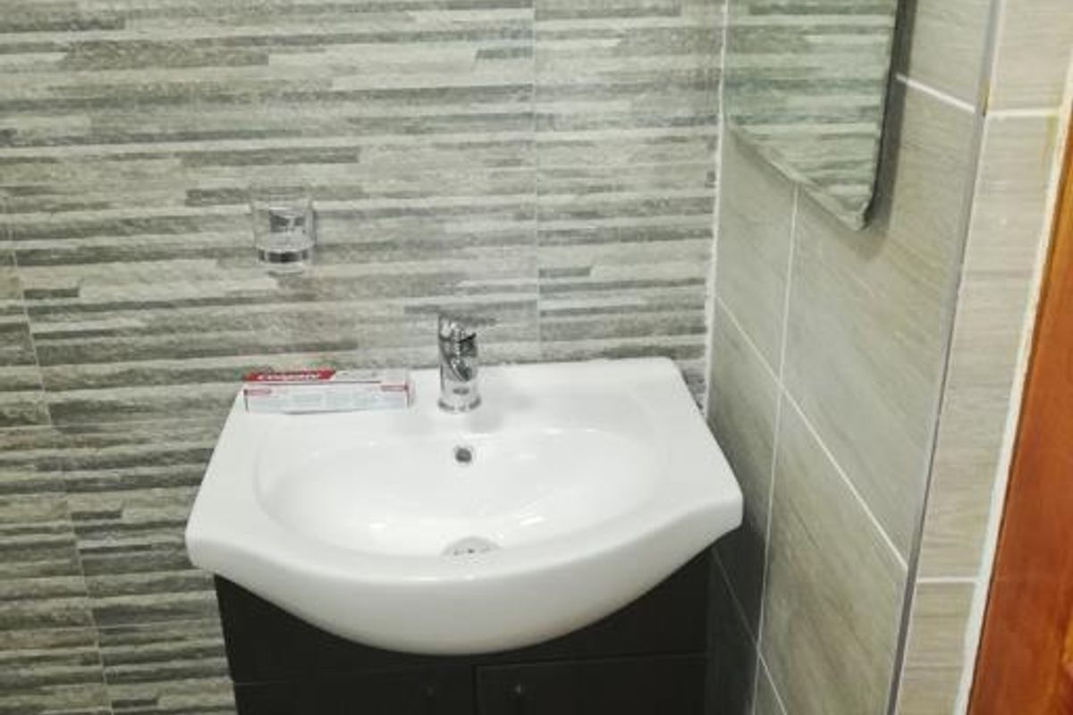 A compact bathroom featuring a modern vanity cabinet with a ceramic basin, mixer tap, and contemporary wall tiling.